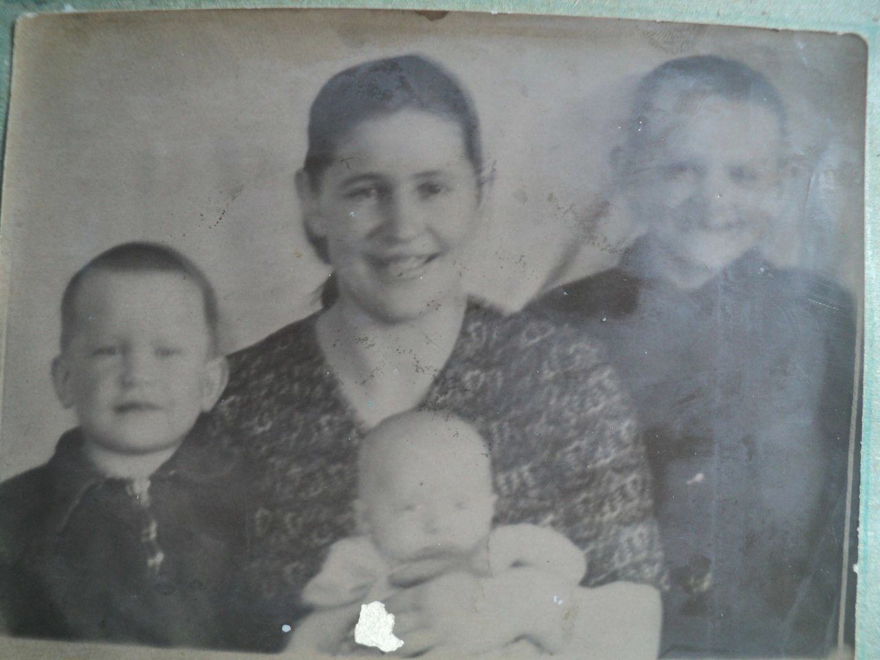 Старая чёрно-белая фотография: улыбающаяся женщина с младенцем на руках, по сторонам от неё двое мальчиков.