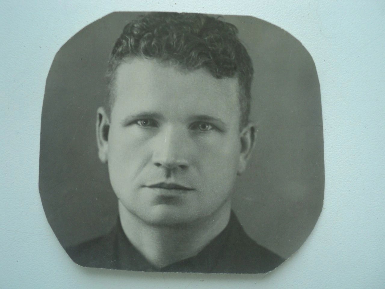 Старая чёрно-белая фотография, обрезанная со скруглёнными углами: мужчина с зачёсанными назад волнистыми волосами, в тёмной рубашке, смотрит прямо в объектив.