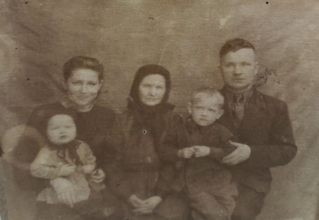 Старая выцветшая фотография в тонах сепии: молодая женщина с младенцем, пожилая женщина в тёмном платке, маленький мальчик и мужчина в тёмном пиджаке.