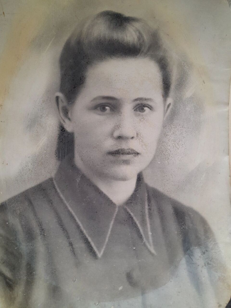 Старая чёрно-белая фотография: молодая женщина с убранными назад волосами, в тёмной блузе с широким отложным воротником.